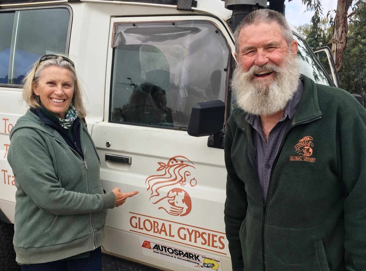 Jan pointing at the Global Gypsies logo on a white tour truck, Jeremy laughing beside her, 2020